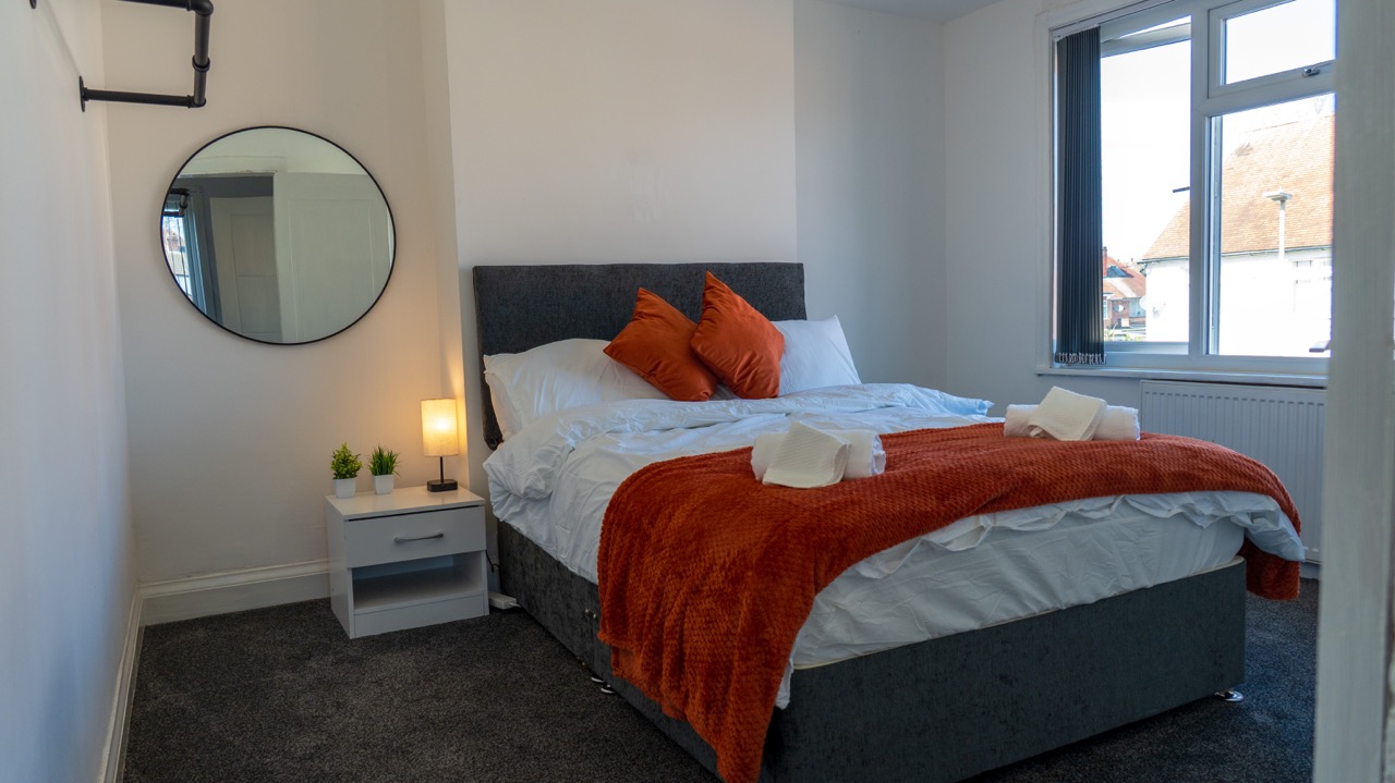 Double bedroom with fresh towels and round mirror at Porlock, Leicester