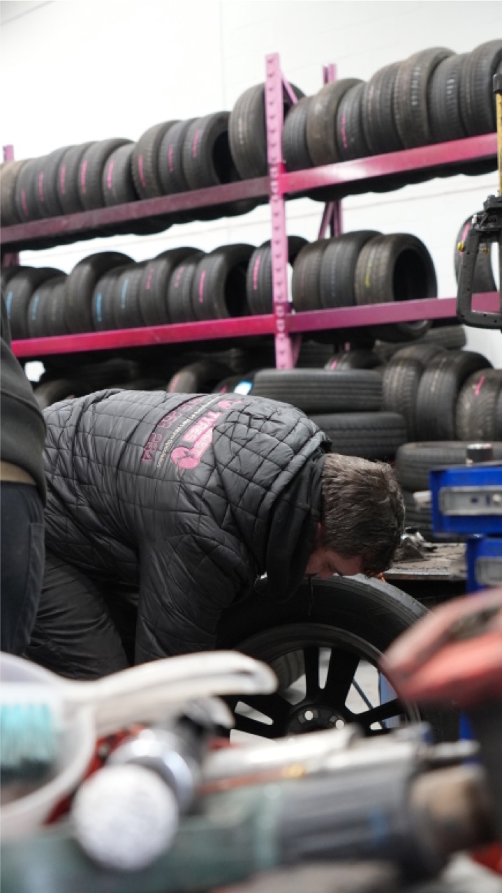 Fitter working on a wheel in front of racked tyres at Low Cost Tyres