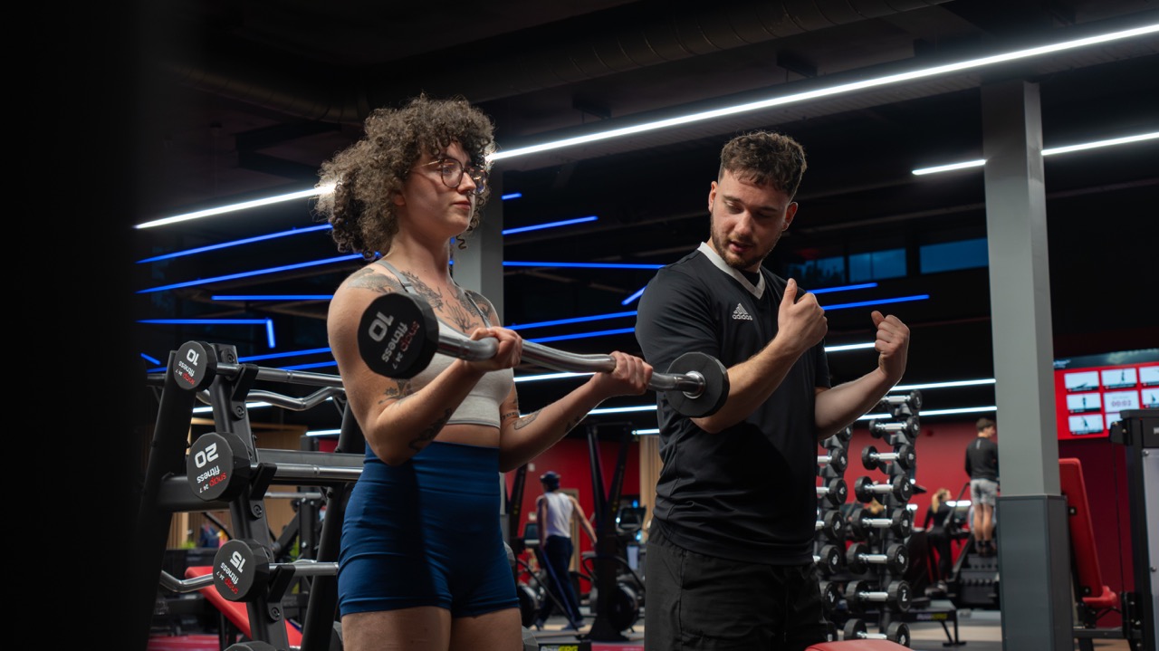 Trainer coaching barbell curl technique on the gym floor