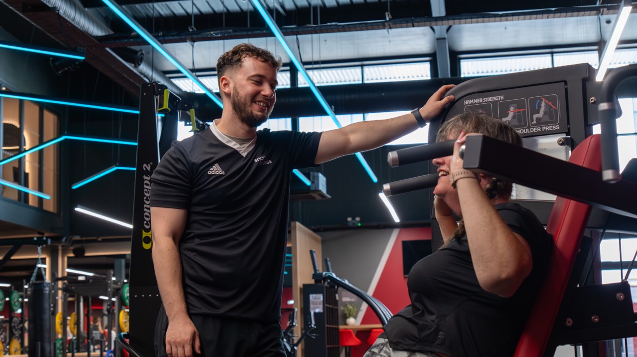 Personal trainer smiling with a client on the shoulder press machine