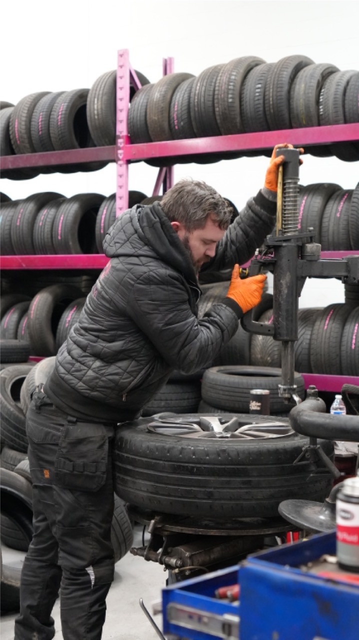 Tyre fitter using the bead breaker beside racks of part-worn tyres