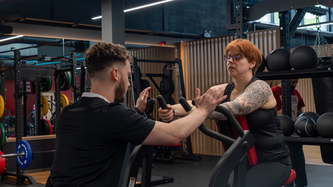 Trainer guiding a client's form on a seated machine