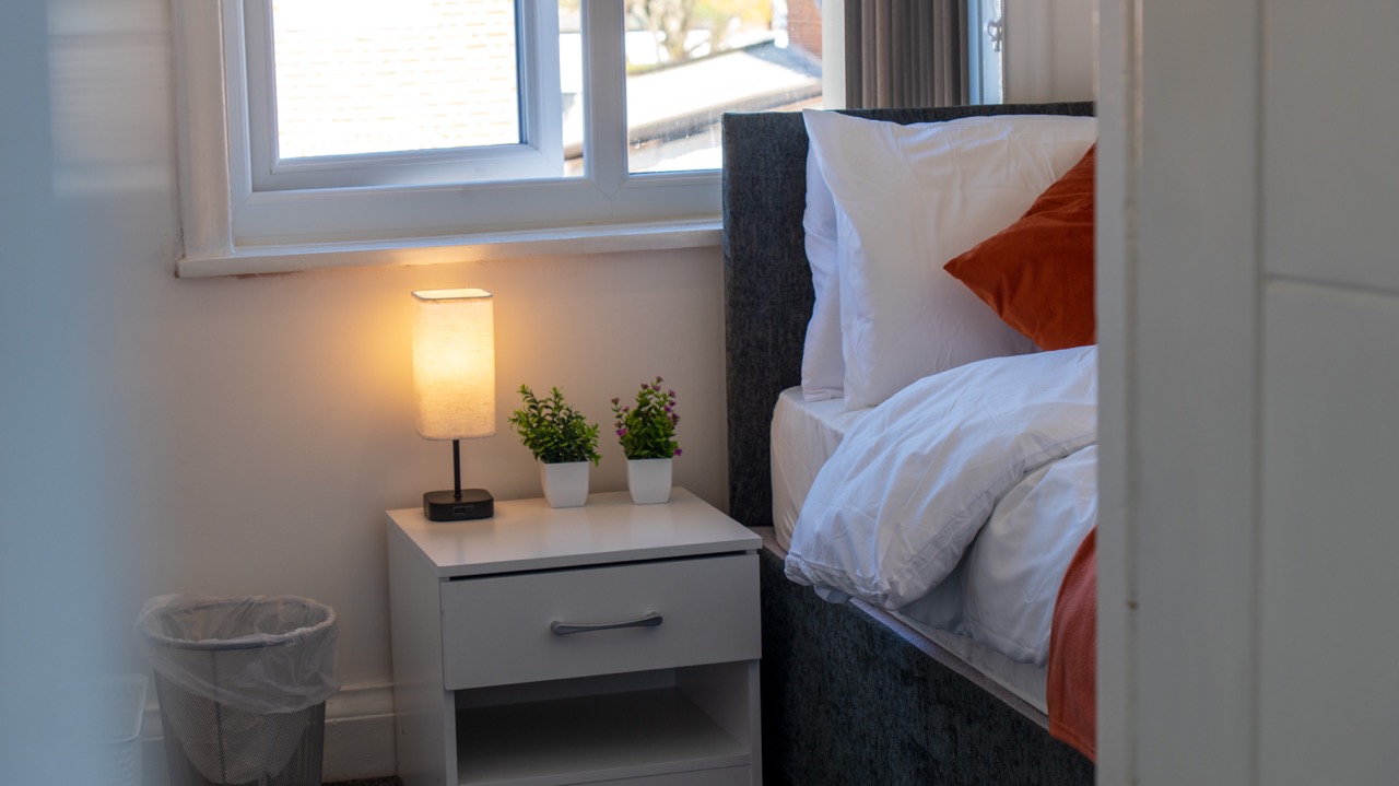 Bedside detail with warm lamp light and crisp white bedding at Porlock, Leicester