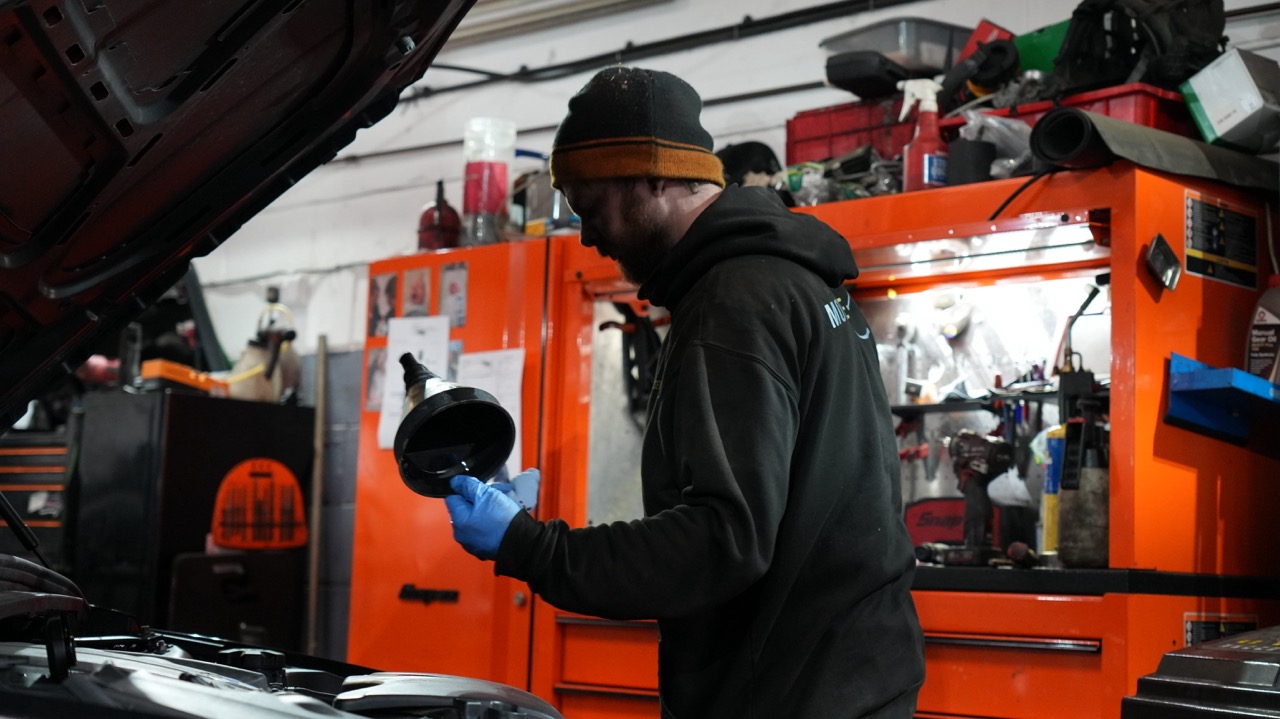 Mechanic with an oil funnel beside an open bonnet at Motor Sense
